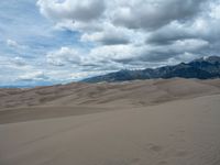 some mountains and grass that is covered in sand dunes on a cloudy day with some clouds