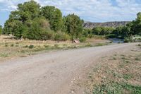 an empty gravel road with dirt and bushes at the side of it and a rusty sign in the background