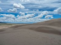 the top of a sandy dune in an open field with blue sky and white clouds