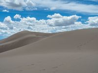 several footprints are left in the sand at an expansive area with rolling hills and clouds