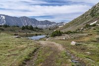 trail running through a mountain meadow in the wilderness with lake and mountains around it with clouds overhead