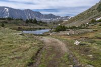 trail running through a mountain meadow in the wilderness with lake and mountains around it with clouds overhead