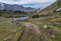 trail running through a mountain meadow in the wilderness with lake and mountains around it with clouds overhead