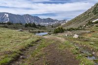 trail running through a mountain meadow in the wilderness with lake and mountains around it with clouds overhead