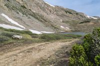 some people walking in the grass near a dirt road with mountains in the background with snow