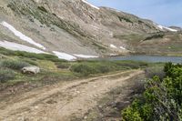 some people walking in the grass near a dirt road with mountains in the background with snow