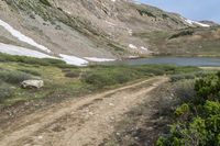 some people walking in the grass near a dirt road with mountains in the background with snow