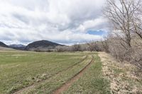 a tractor tracks is shown near grass and trees in the distance is mountains, clouds, and blue sky