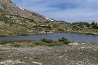 a green meadow near the mountains with a body of water under it and lots of rocks