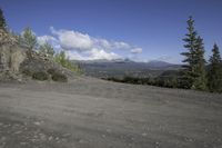 a mountain side road with a large rock cliff in the background as clouds move across the blue sky