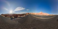 a very wide lens of the road with clouds and mountains in the background and a man riding on the side of the road