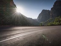 a wide highway next to mountains with a road running beside it and sun shining through the top