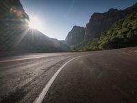 a wide highway next to mountains with a road running beside it and sun shining through the top