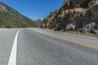 an empty open highway passing through the mountains, near a mountain and a pine forest