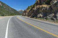 an empty open highway passing through the mountains, near a mountain and a pine forest