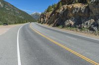 an empty open highway passing through the mountains, near a mountain and a pine forest