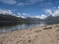 a lake with rocks on the shore and mountains in the background along side it and snow capped hills