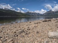 a lake with rocks on the shore and mountains in the background along side it and snow capped hills