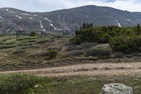 a person on a bike stands on a trail in the mountains with a view of a mountain range