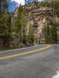 the curved road curves in front of a mountain area with pine trees behind it,