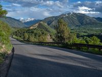 the road winds up on the mountainside on a sunny day with beautiful clouds and trees