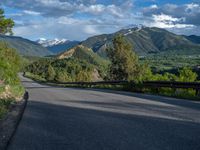 the road winds up on the mountainside on a sunny day with beautiful clouds and trees