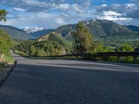 the road winds up on the mountainside on a sunny day with beautiful clouds and trees