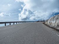 a snow covered road is near a very steep cliff on a clear day the wall is filled with snow and snow