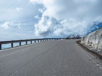 a snow covered road is near a very steep cliff on a clear day the wall is filled with snow and snow