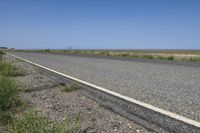 an empty roadway with a road sign on the side of the road near the grass and a clear blue sky