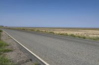 an empty roadway with a road sign on the side of the road near the grass and a clear blue sky