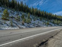 an empty highway is surrounded by evergreens and snow on the side of a hill