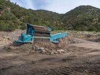 two yellow bulldozers work on sand and gravel in a mountain valley while another one looks at it