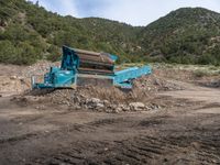 two yellow bulldozers work on sand and gravel in a mountain valley while another one looks at it