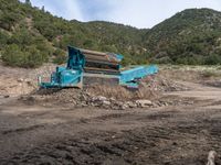 two yellow bulldozers work on sand and gravel in a mountain valley while another one looks at it