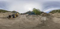 a big tractor parked in front of a dump truck at a construction site near some mountains