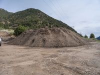 two yellow bulldozers work on sand and gravel in a mountain valley while another one looks at it