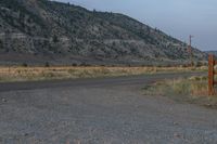 the street is empty and dirt covered by rocks and weeds while the mountain is in the distance