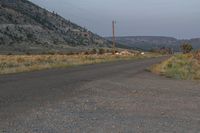 the street is empty and dirt covered by rocks and weeds while the mountain is in the distance