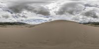 the large sand hill in the middle of a large desert area with mountains in the background