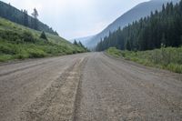 a view of an empty dirt road near the mountains near the trees on a cloudy day