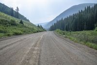 a view of an empty dirt road near the mountains near the trees on a cloudy day