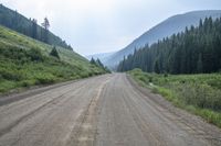 a view of an empty dirt road near the mountains near the trees on a cloudy day