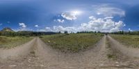 a panorama photo of two trails going between the grass and a mountain range in the distance