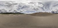 a panorama of desert sand dunes with large cloud formation over mountains in the background by john wyke