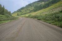 a long dirt road with grass and trees behind it and mountains in the distance on a sunny day