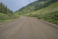 a long dirt road with grass and trees behind it and mountains in the distance on a sunny day