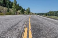 a long highway that has some yellow stripes and trees in the background while the road is gray