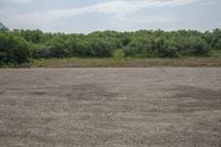 a man walking across an empty field towards a forest covered area holding a kite in his hand