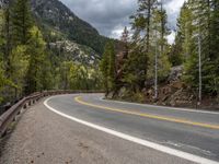 the curved road curves in front of a mountain area with pine trees behind it,